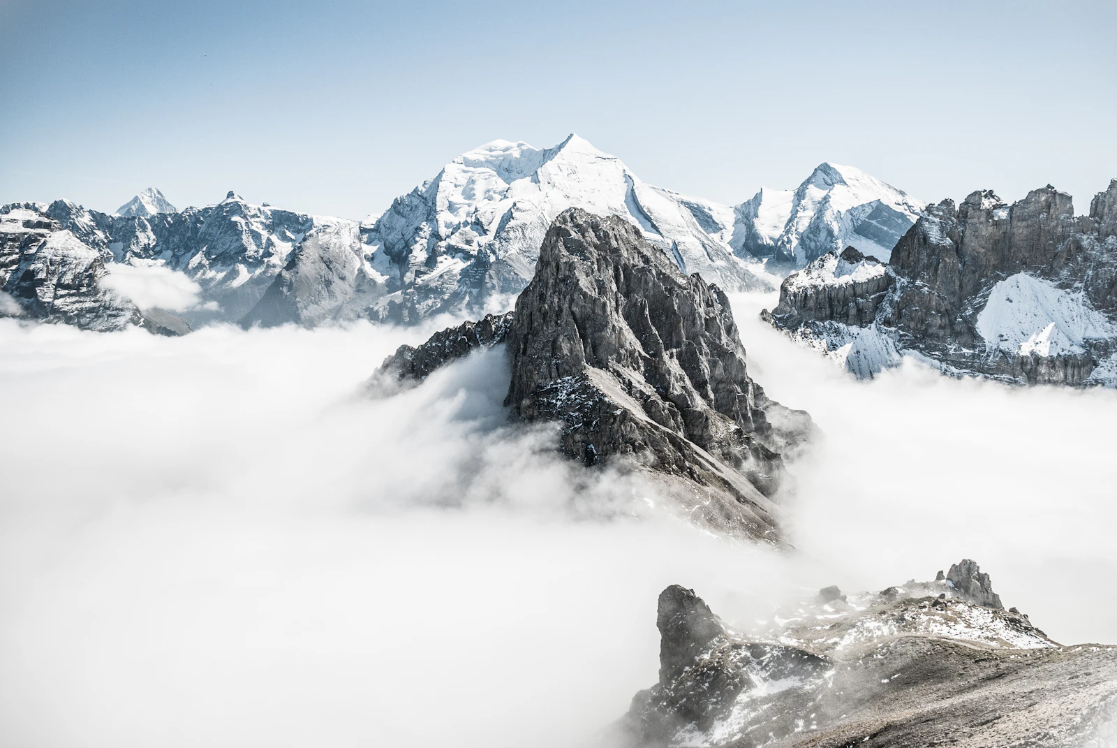 A rocky summit piercing a sea of clouds among snowy peaks