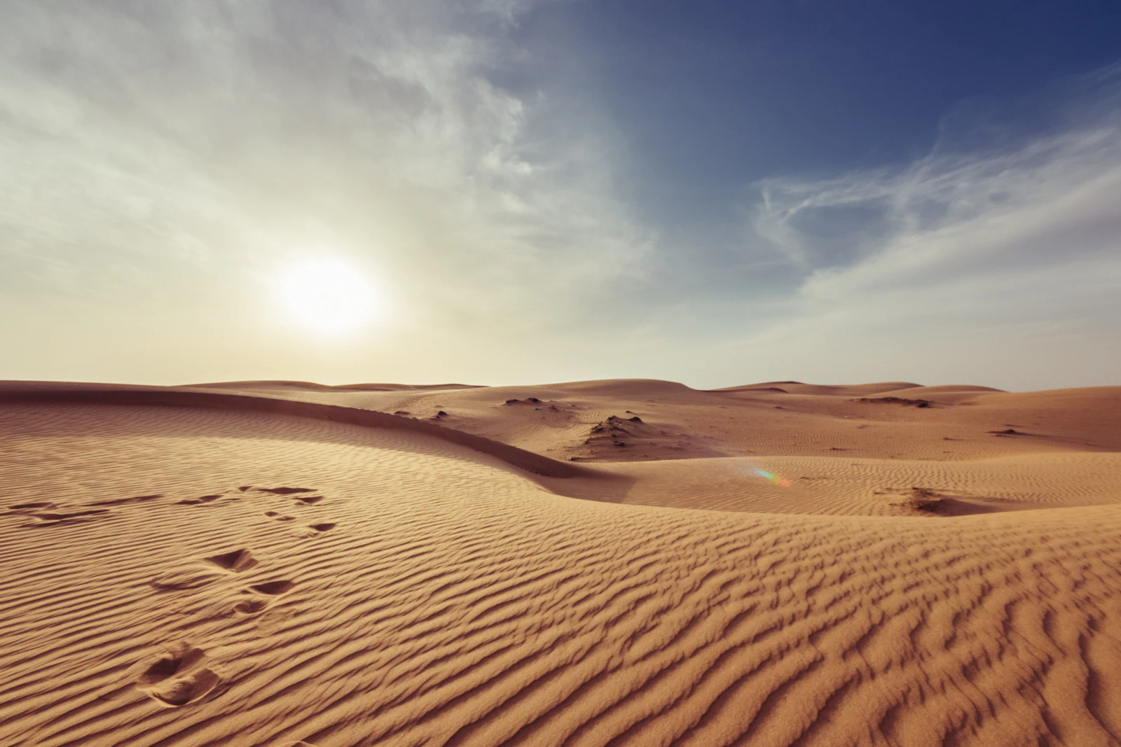 Footprints crossing rippled desert dunes under a hazy midday sun