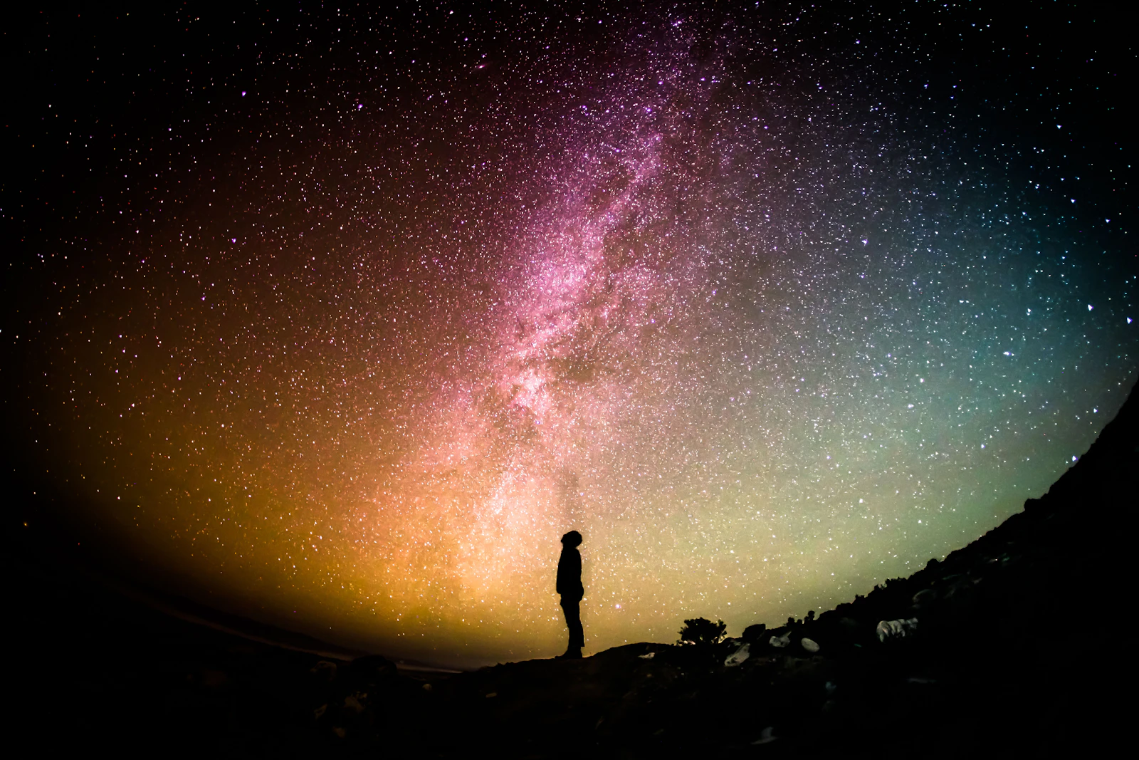 A lone figure standing under the Milky Way in a fisheye night sky